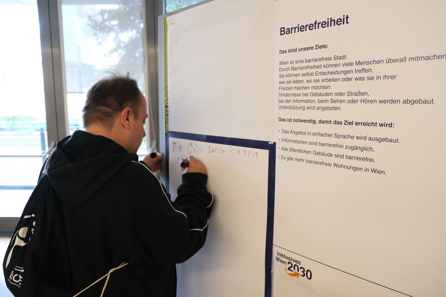 Ein Teilnehmer schreibt seine Rückmeldung zum Thema Barrierefreiheit auf ein Plakat.